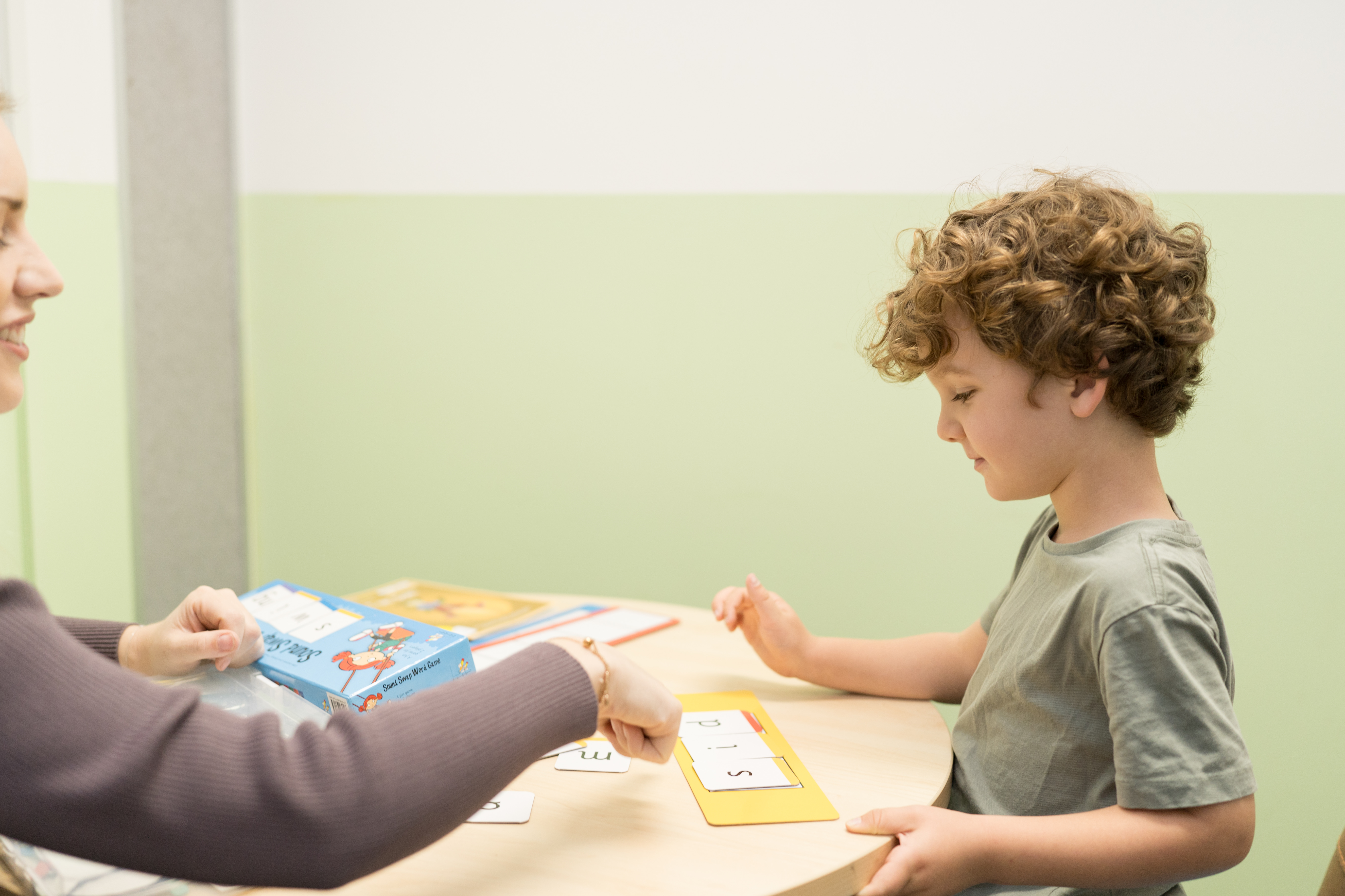 A child working through letter sounds with letter cards at the table, guided by their speech pathologist